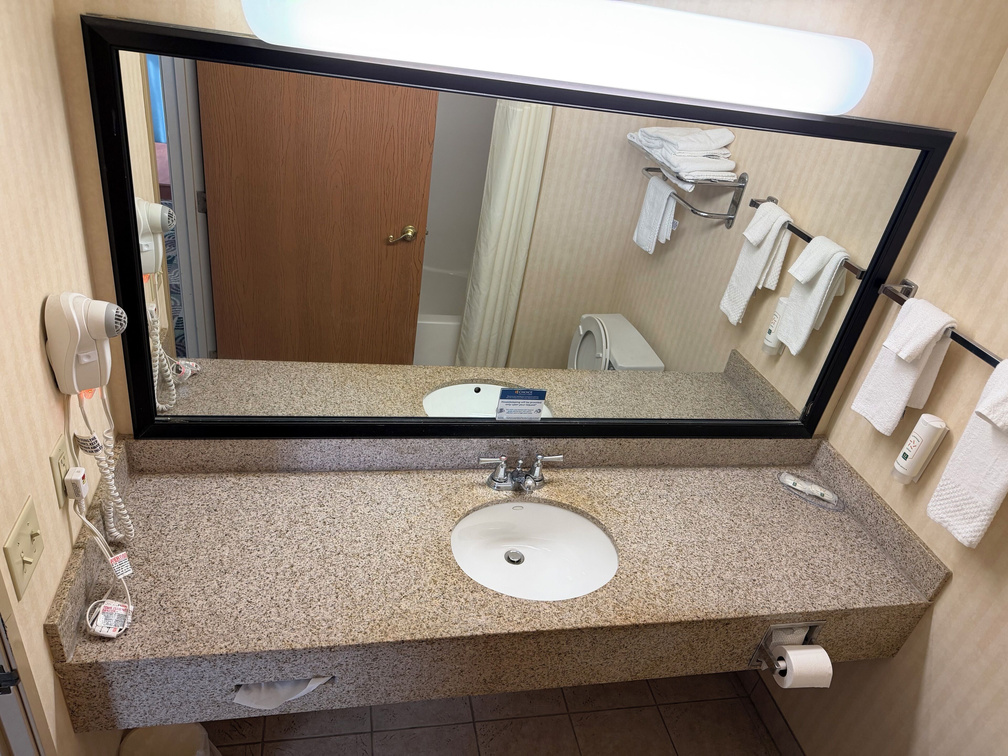 A bathroom with a granite countertop, a sink, a mirror, a towel rack, and a hairdryer.