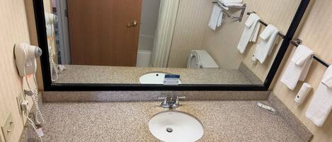 A bathroom with a granite countertop, a sink, a mirror, a towel rack, and a hairdryer.