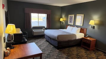 A hotel room with a bed, bedside tables, a desk, a chair, a window with curtains, wall-mounted lamps, and a wall-mounted air conditioner.