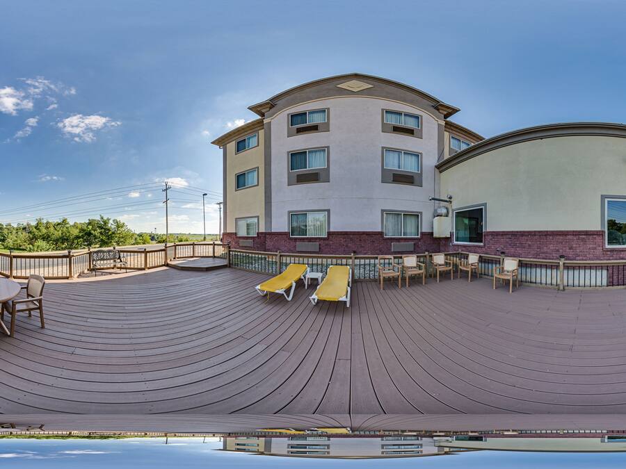 Un hotel con terraza de piscina, mobiliario exterior y un edificio grande con muchas ventanas.