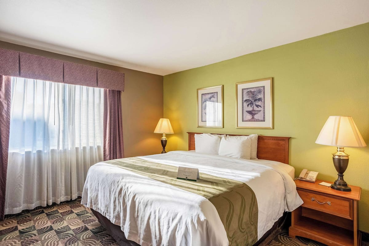 A hotel room with a large bed, two bedside lamps, a nightstand, and a window with curtains.