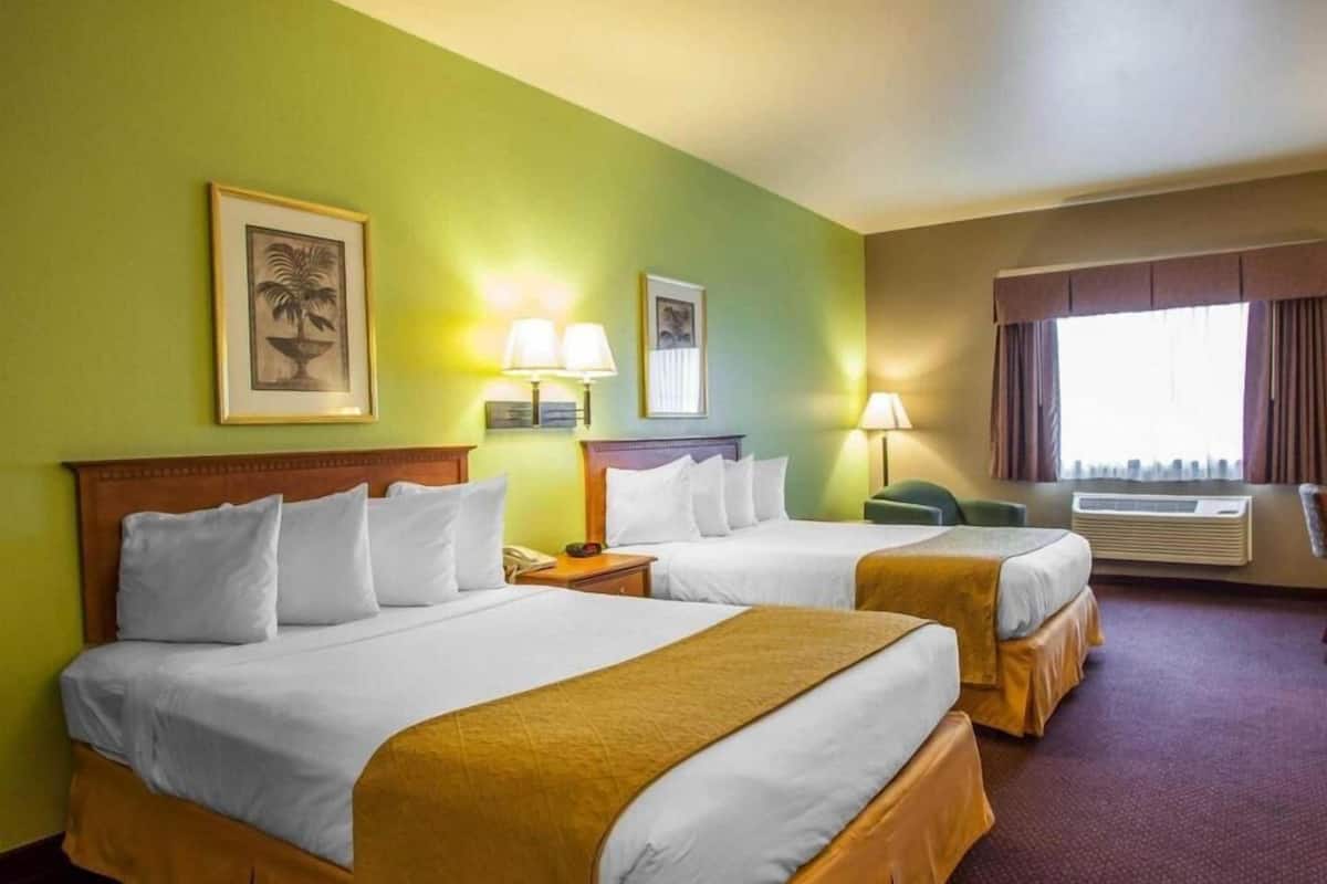 A hotel room with two beds, a green wall, framed artwork, and an air conditioning unit.