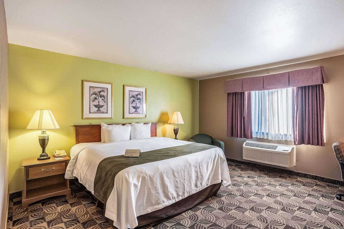 A hotel room with a bed, two bedside lamps, a nightstand, a chair, and a window with curtains.
