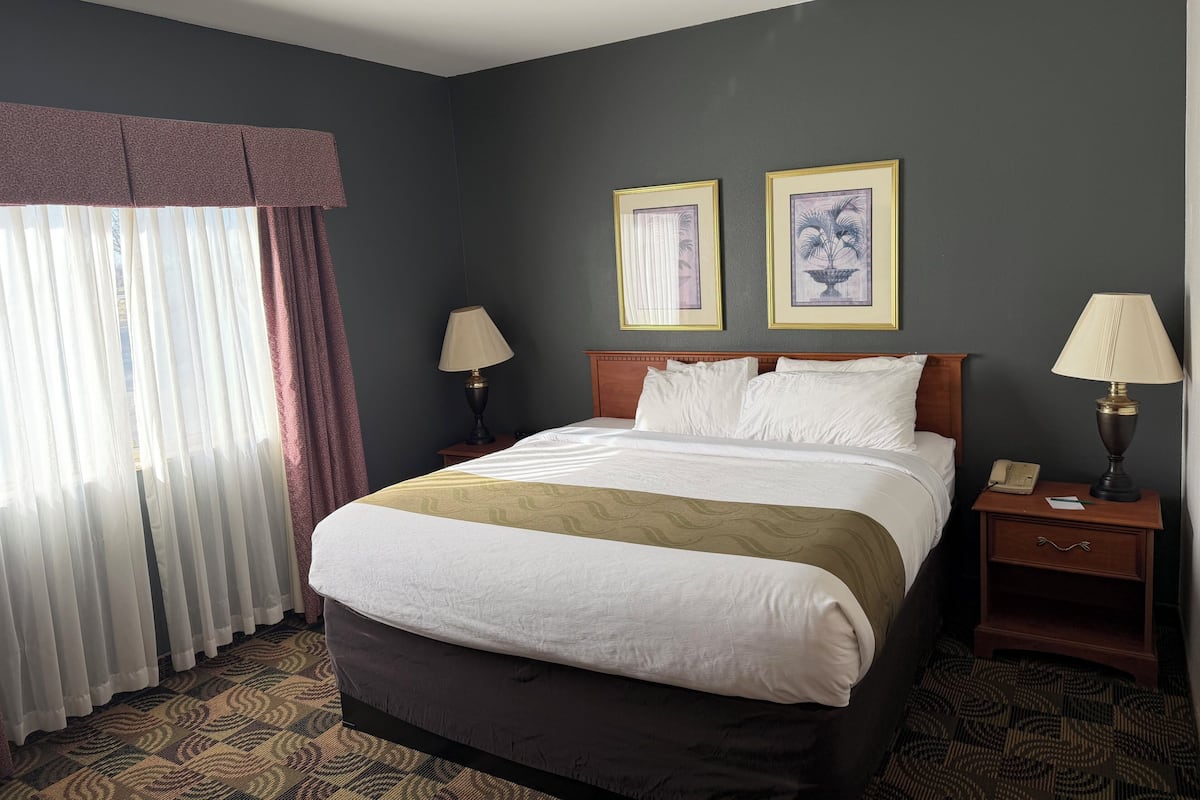 A hotel room with a bed, two bedside tables, a nightstand, a telephone, and two framed pictures on the wall.