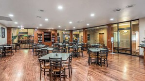 A spacious dining area with wooden flooring and tables, surrounded by glass walls and wooden paneling.