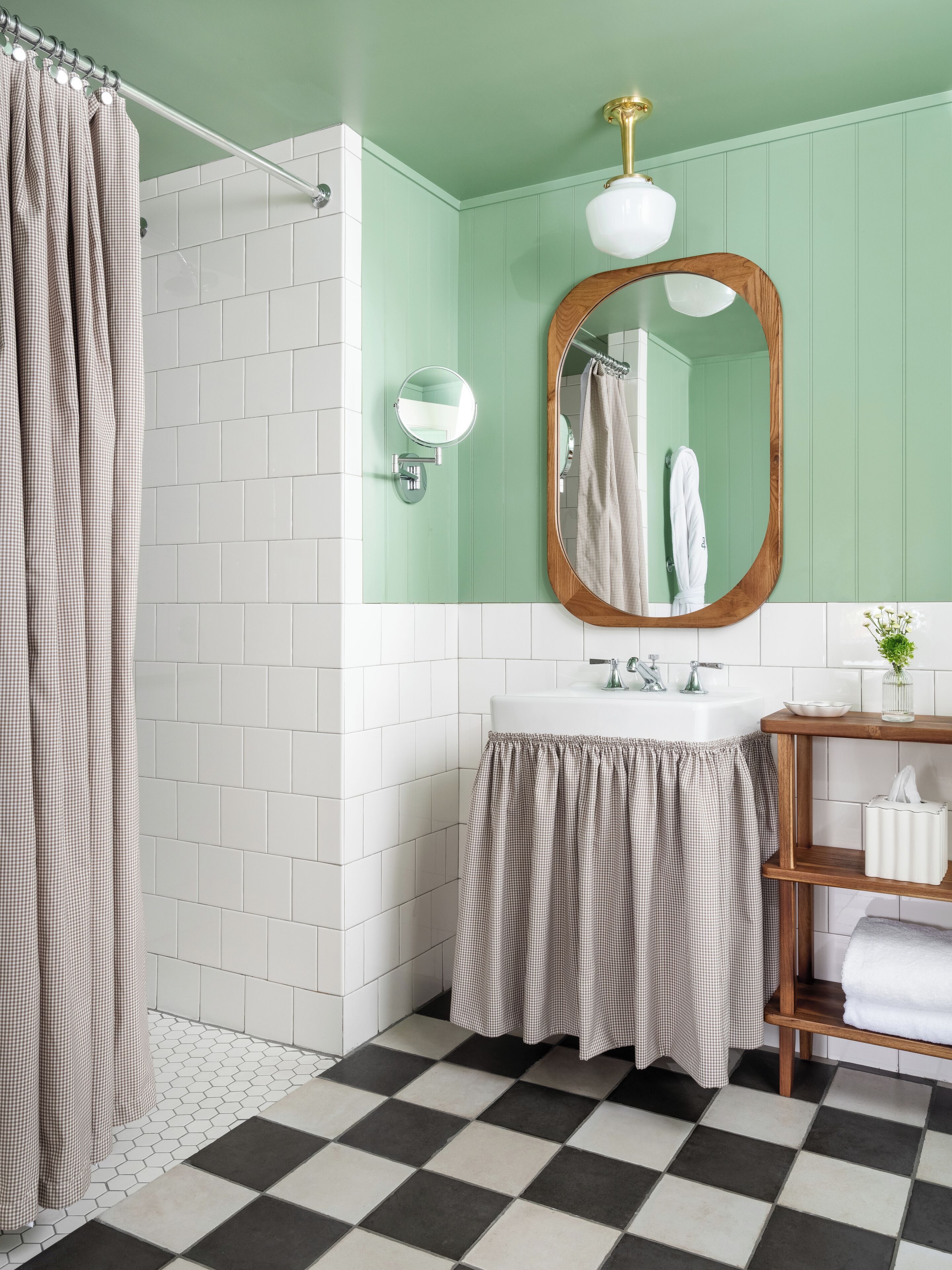A bathroom with a checkered shower curtain, a round mirror, a white sink, and a wooden shelf with a towel.