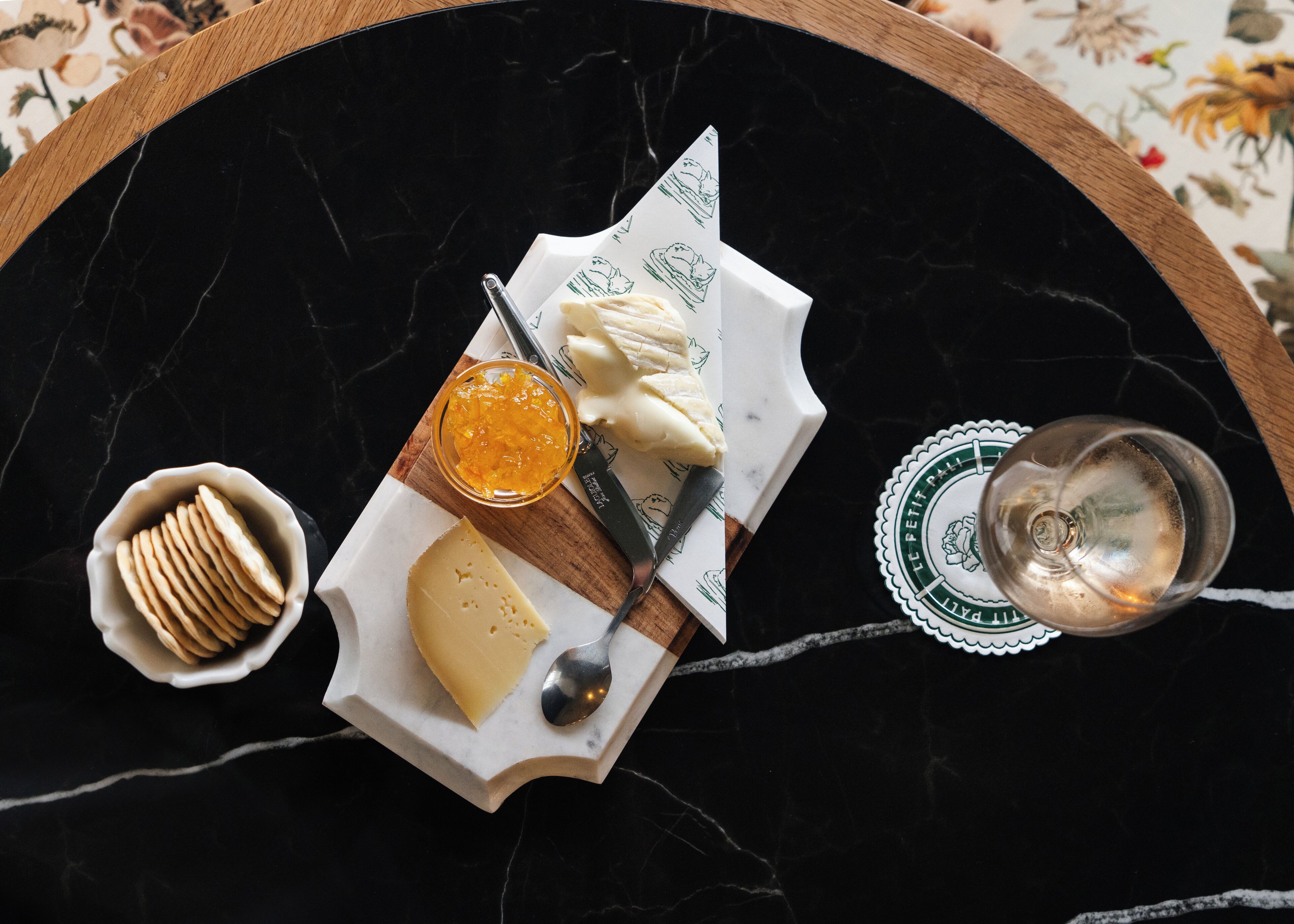 A cheese board with crackers and a glass of water on a marble table.