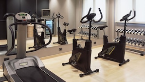 A gym with cardio machines, a mirrored wall, and a rack of dumbbells. - Hotel Ciutat Martorell (Martorell)