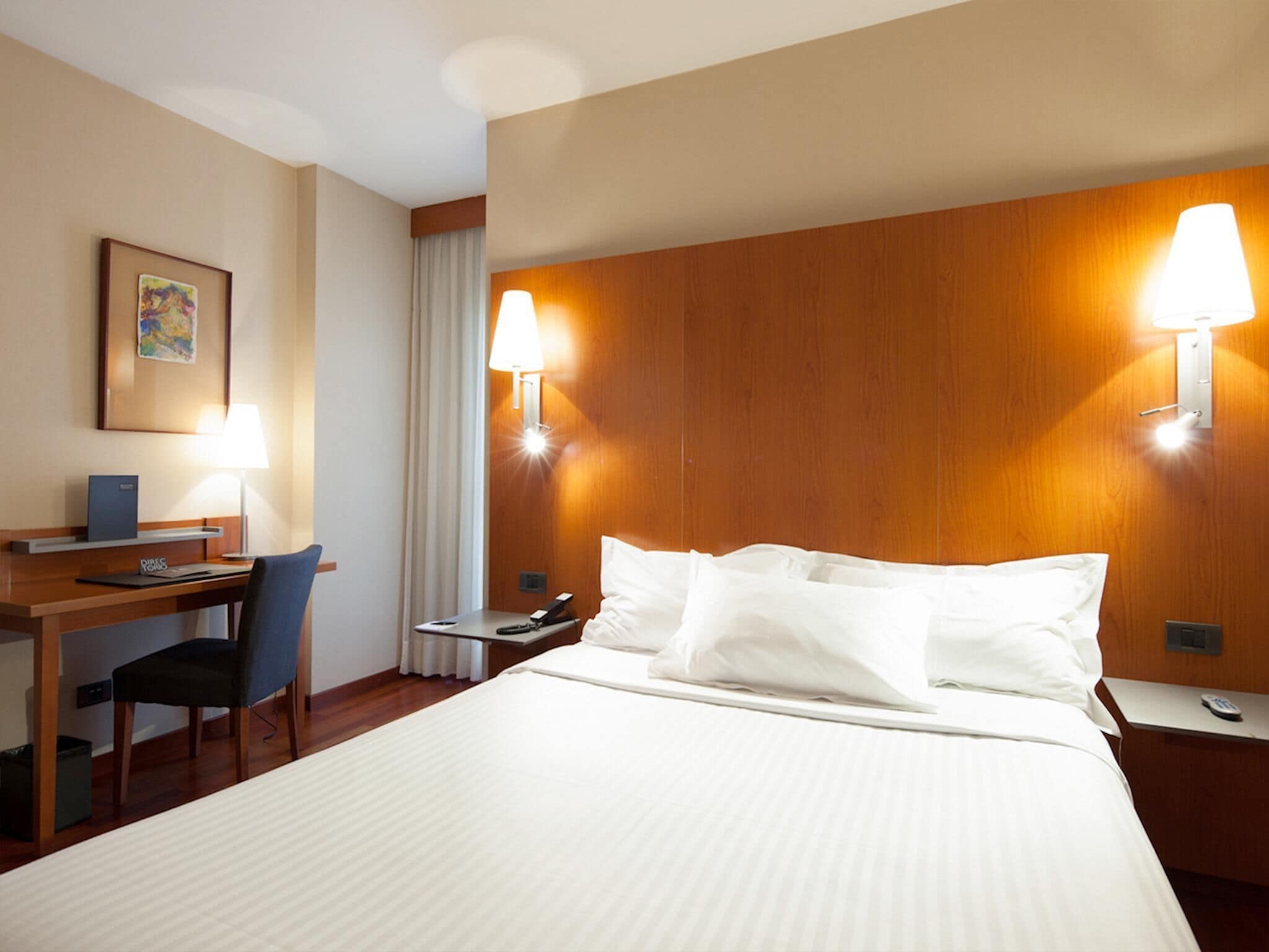 Een hotelkamer met een bed, bureau, stoel en twee wandlampen.