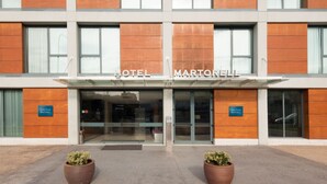 A modern hotel building with a prominent 'HOTEL MARTORELL' sign above the entrance. There are two large potted plants in front of the entrance. - Hotel Ciutat Martorell (Martorell)