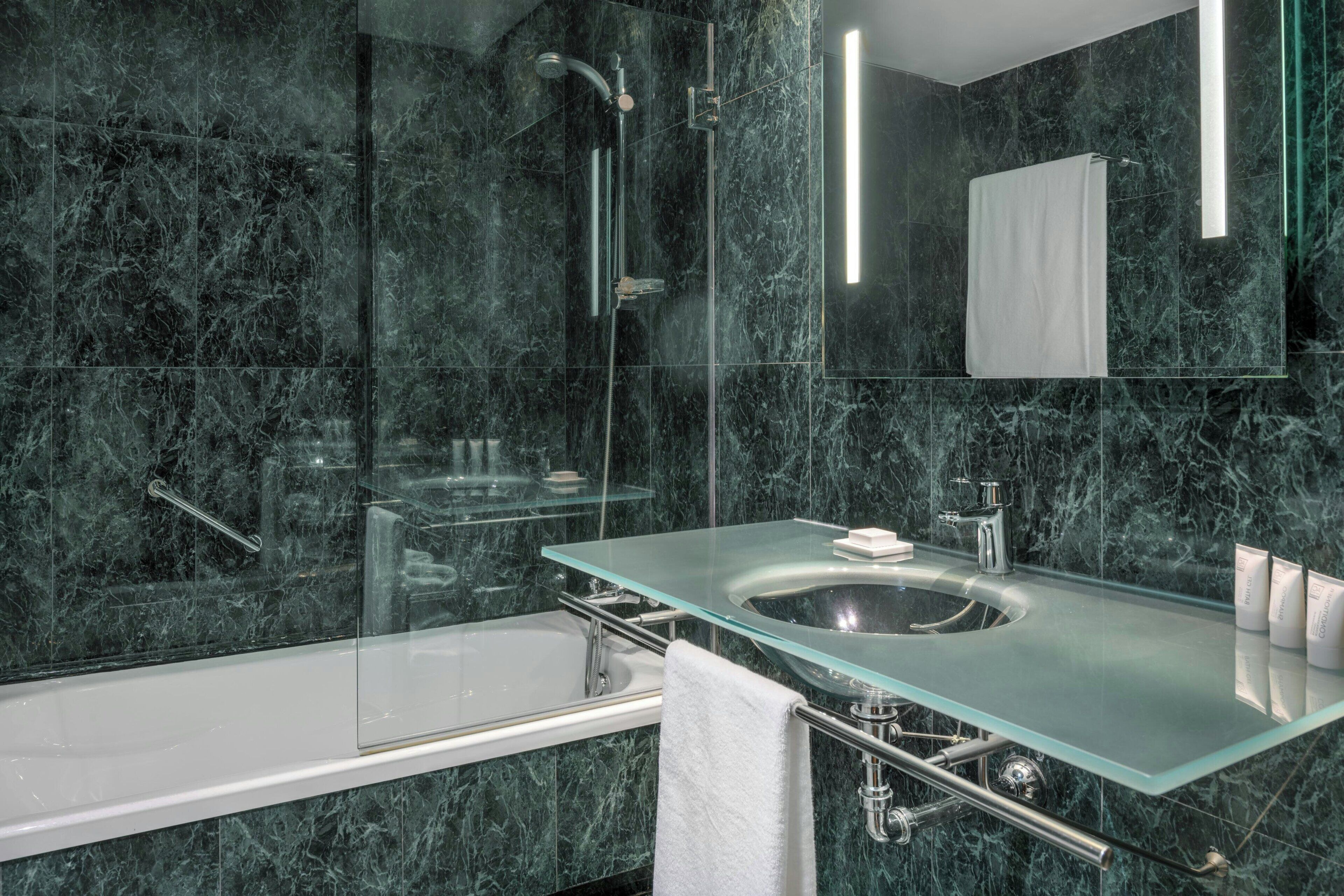 Un baño moderno con lavamanos de vidrio, bañera y ducha con cerramiento de vidrio.