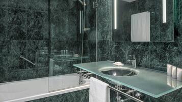 Un baño moderno con lavamanos de vidrio, bañera y ducha con cerramiento de vidrio.