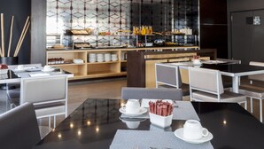 A modern dining area with a glass partition, buffet with various food items, and seating arrangements. - AC Hotel Elda by Marriott (Elda)