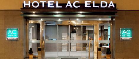 The entrance to HOTEL AC ELDA with a glass door and a sign above.