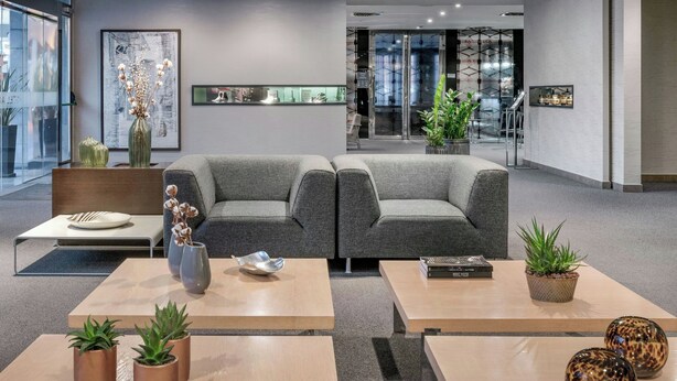 A modern lobby with grey sofas, a reception desk, and a coffee table with plants. - AC Hotel Elda by Marriott (Elda)