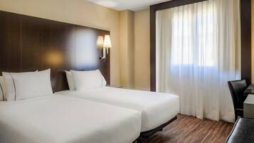 Habitación de hotel con dos camas, un escritorio, una silla y un ventanal con cortinas.
