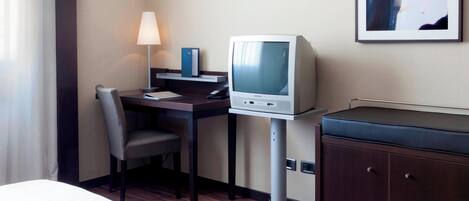 A hotel room with a desk, chair, television, and a cabinet.