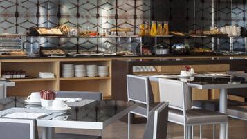 Un café moderno con mesas y sillas de vidrio, un mostrador de buffet con diversas opciones de comida y una pared con diseño.