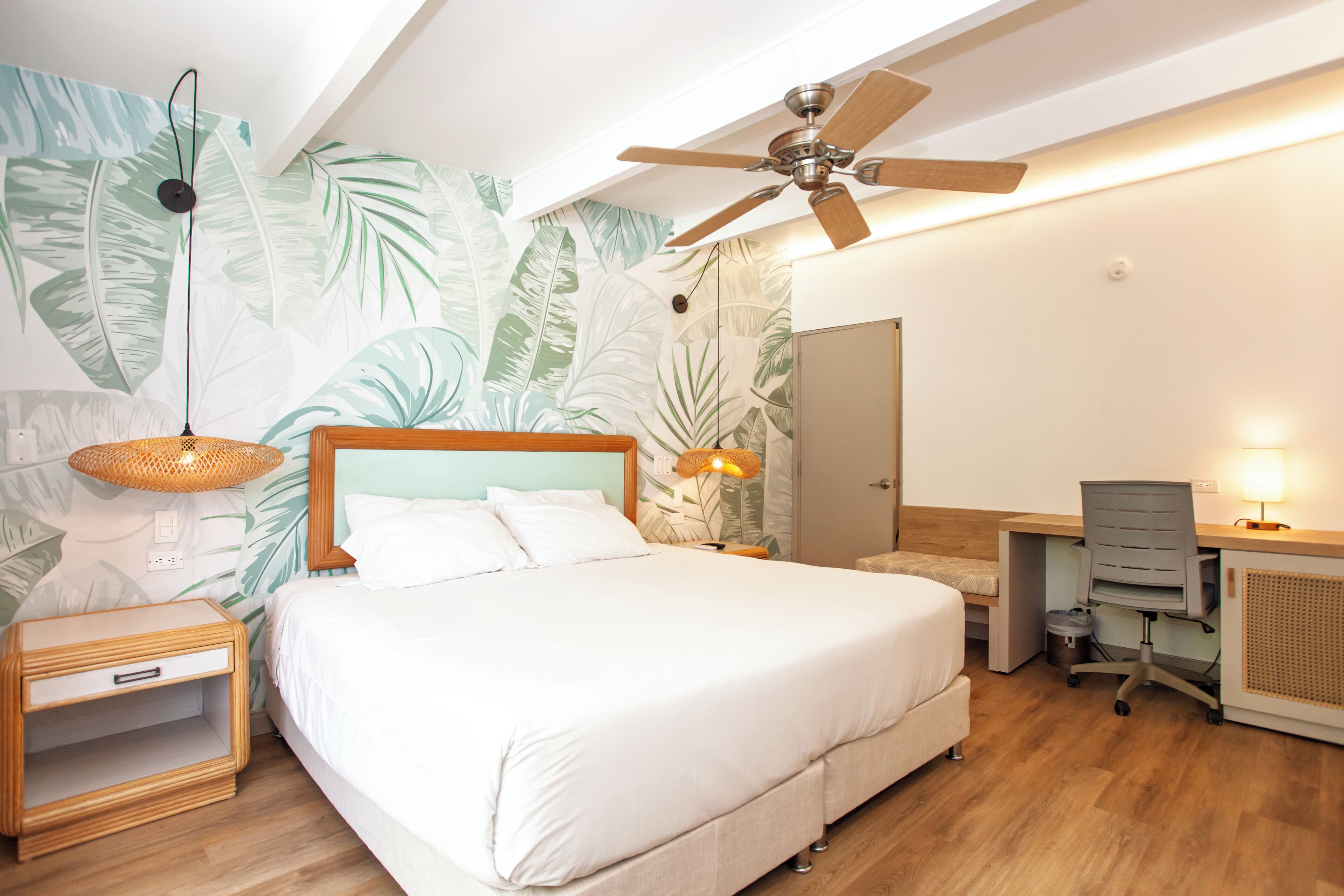 A bedroom with a bed, a desk, a chair, a ceiling fan, and a wall with a leaf pattern.