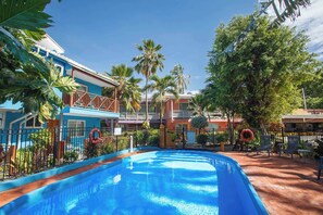 A swimming pool surrounded by a fenced area with palm trees and a building with a balcony. - Cocoplum Beach Hotel (San Andrés)
