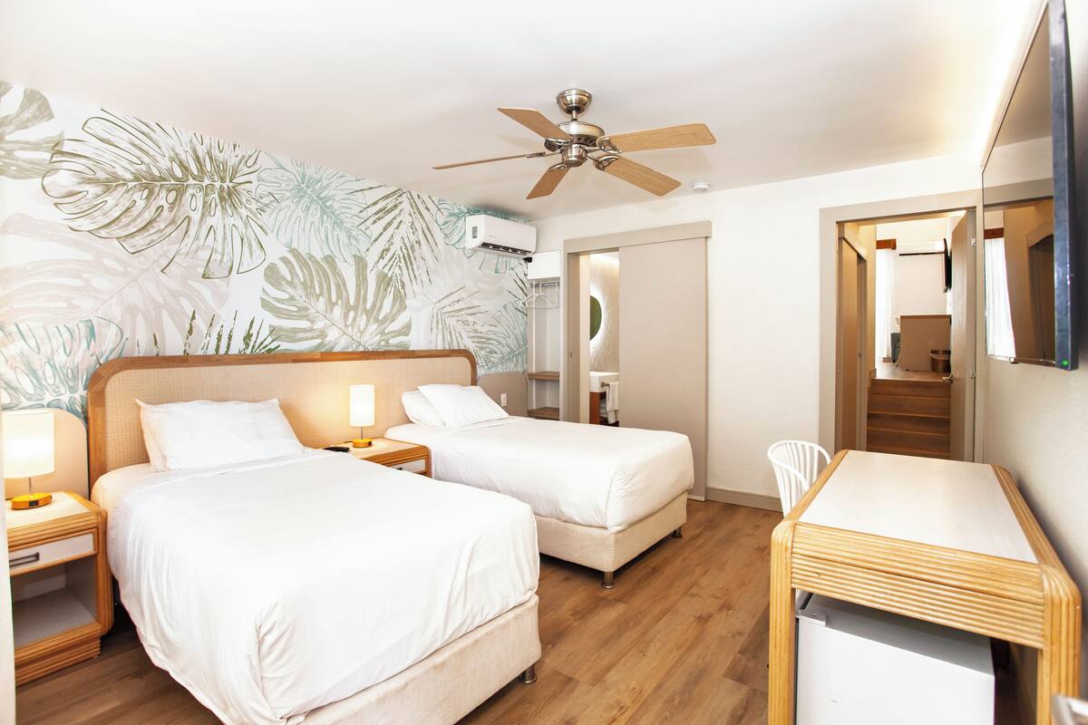 Habitación de hotel con dos camas, un escritorio, un ventilador de techo y un mural grande en la pared.