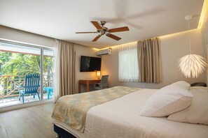 A hotel room with a bed, a ceiling fan, a TV, a desk with a chair, and a balcony with a chair and table.