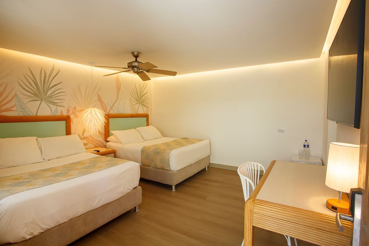 A hotel room with two beds, a ceiling fan, a desk with a chair, and a TV.