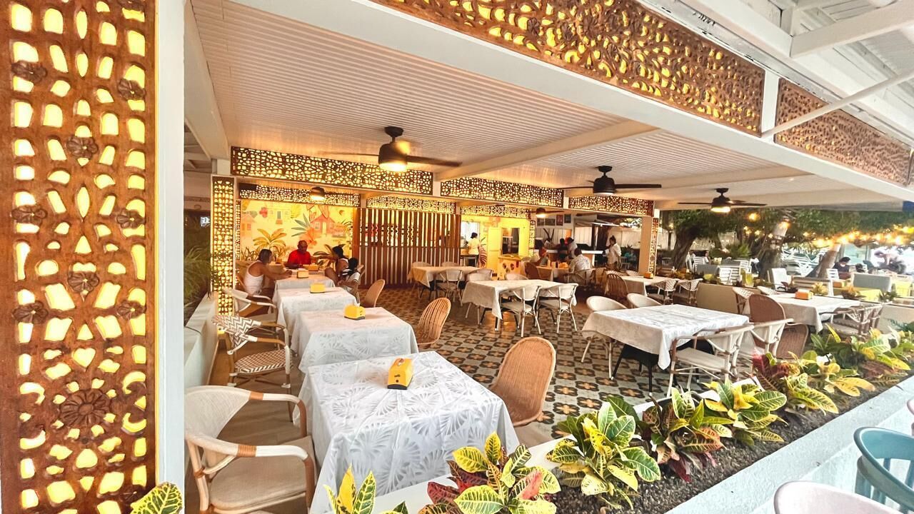 Un restaurante al aire libre con mesas, sillas, paneles decorativos y plantas.