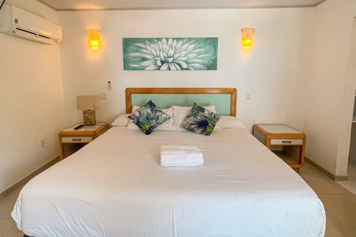 Habitación de hotel con una cama, dos mesitas de noche, un ventilador de techo y un aire acondicionado montado en la pared.