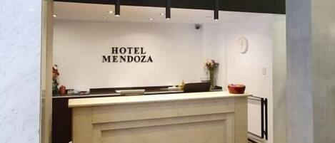 A hotel reception area with a marble floor, a wooden slatted ceiling, and a reception desk labeled "HOTEL MENDOZA".