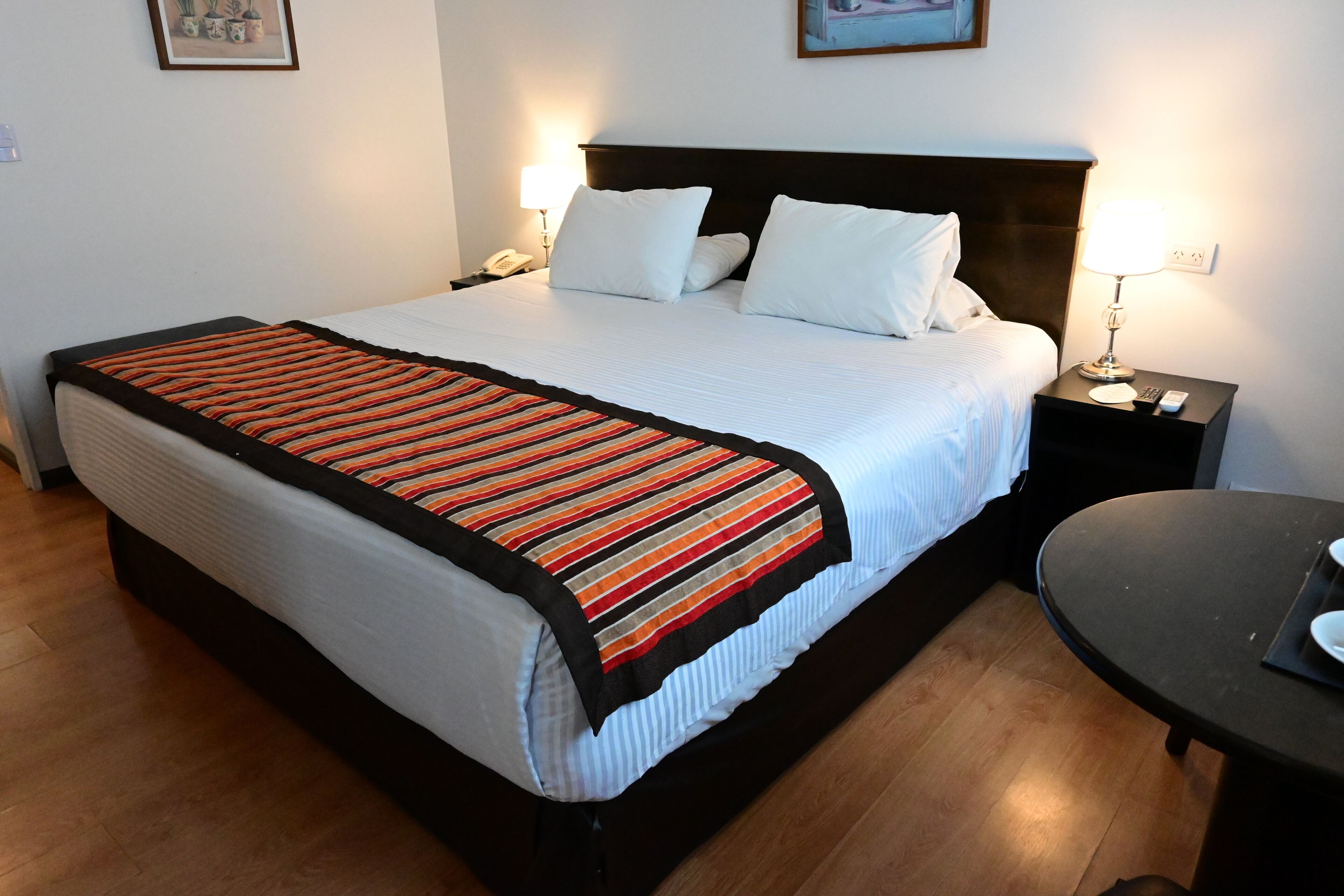 A neatly made bed with a striped blanket, a bedside table with a lamp, and a small round table.