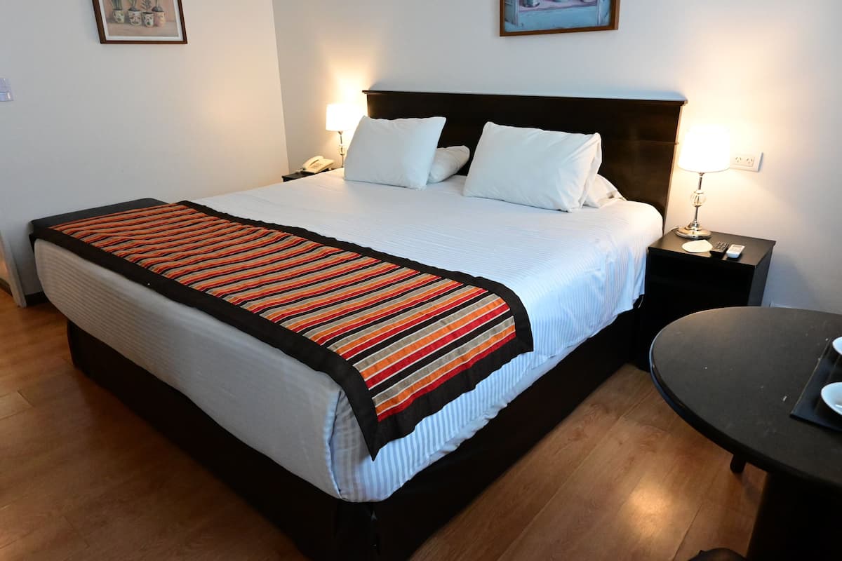 A neatly made bed with a striped blanket, a bedside table with a lamp, and a small round table.