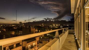 Un balcón con vista a la ciudad al atardecer, con edificios modernos y cielo despejado.
