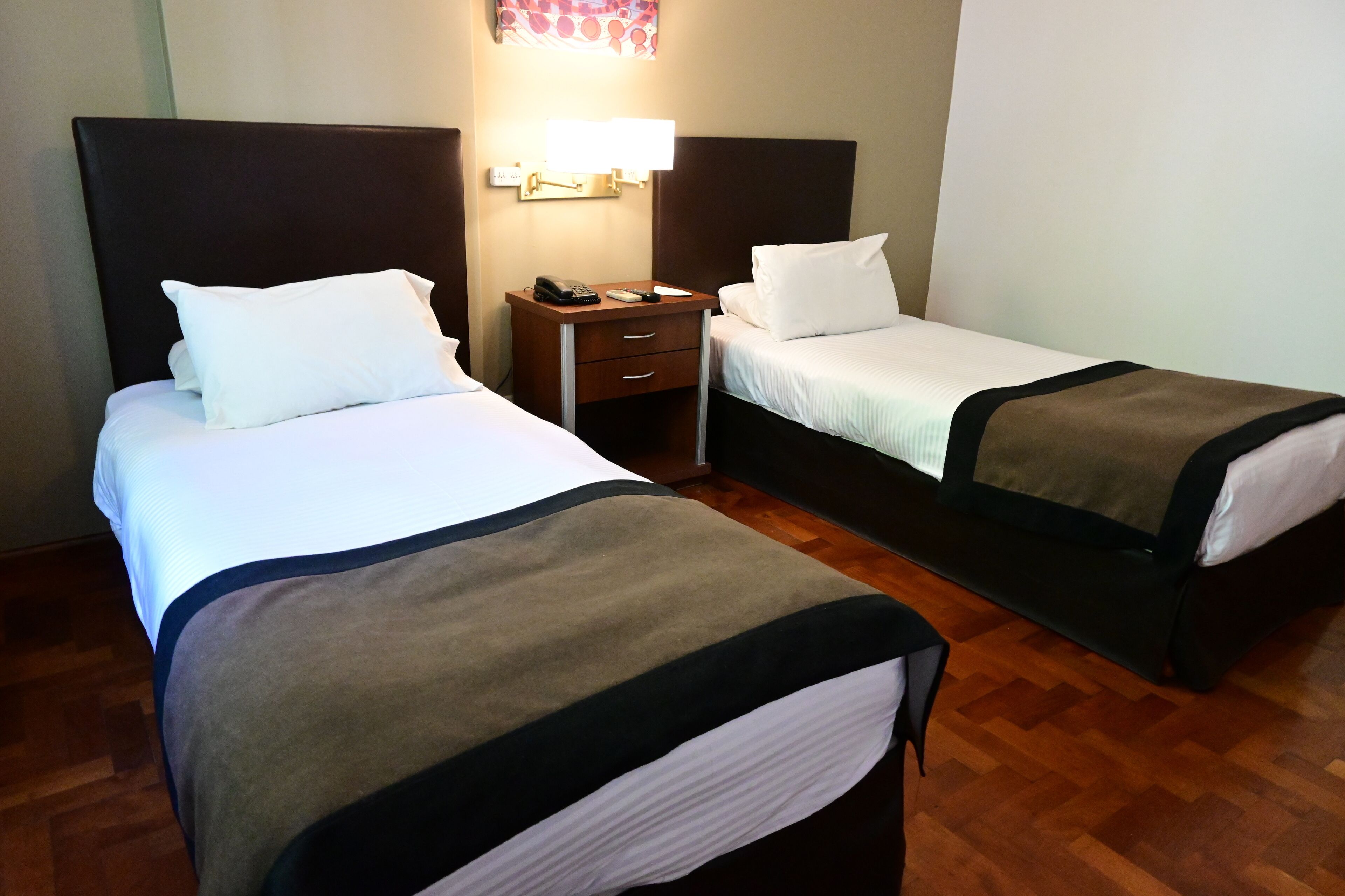 Quarto de hotel com duas camas, uma mesa de cabeceira com telefone e uma luminária fixada na parede.