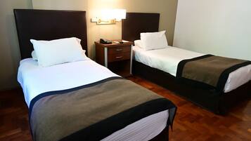 Quarto de hotel com duas camas, uma mesa de cabeceira com telefone e uma luminária fixada na parede.
