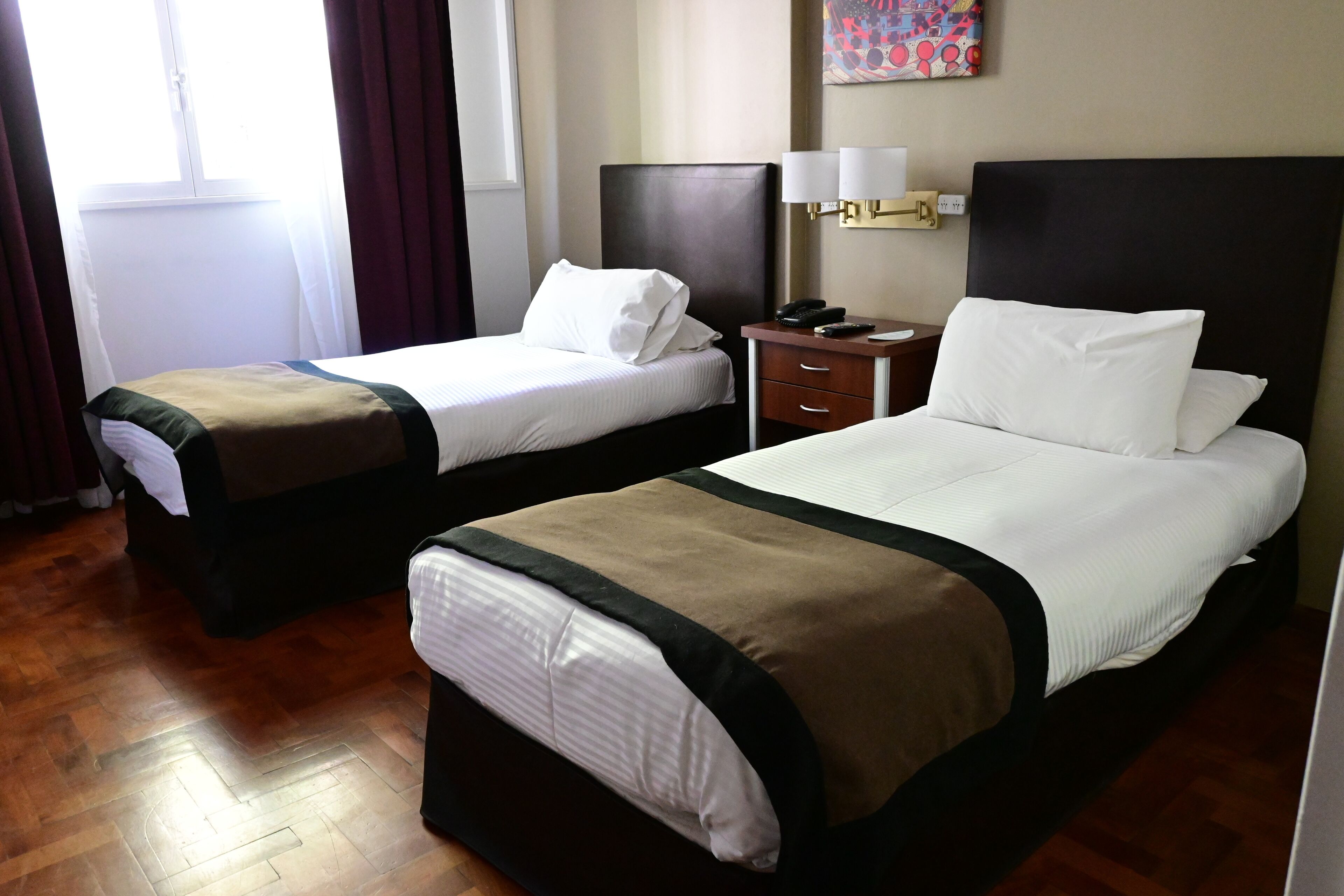 A hotel room with two beds, a nightstand with a lamp, and a painting on the wall.