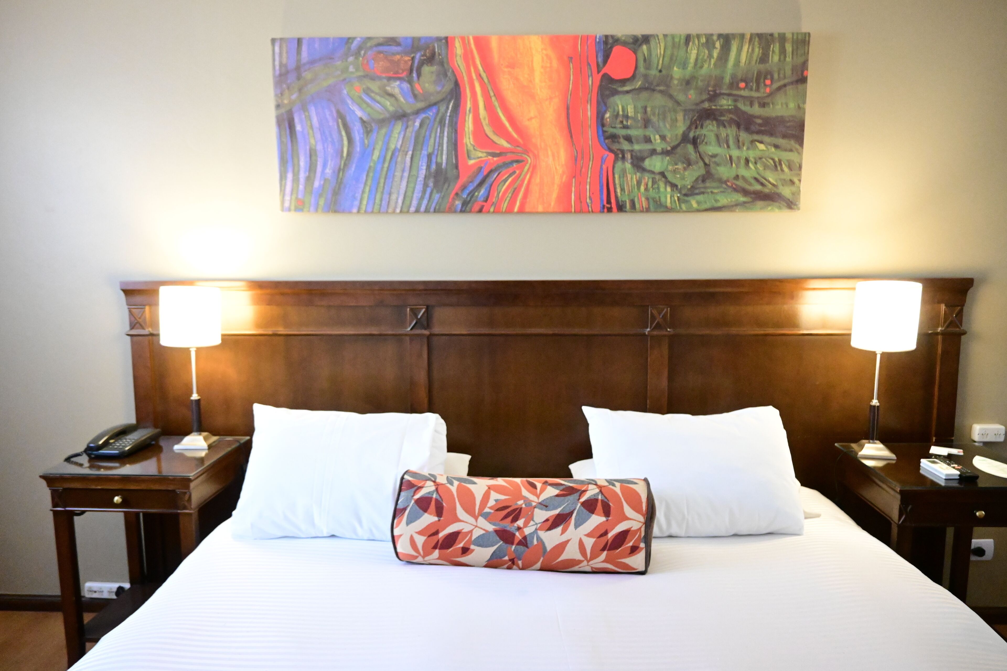 Une chambre d’hôtel avec un grand lit, deux lampes de chevet, un téléphone et un tableau au mur.