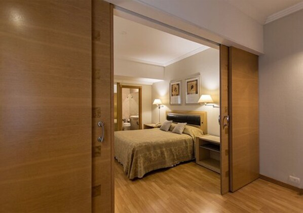 Una habitación de hotel con suelo de madera, una cama con cabecero, mesitas de noche con lámparas y un armario.