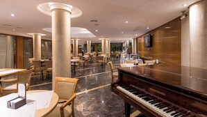 Un amplio vestíbulo de hotel con un piano de cola, varias mesas de comedor y una zona de bar.