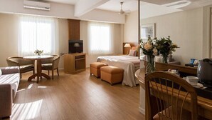 Habitación de hotel con cama, escritorio, silla, televisor, cafetera y espejo.