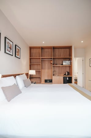 A bedroom with a large bed, wooden shelving, a microwave, and a small refrigerator.