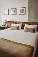 A hotel room with a large bed, wooden headboard, two bedside tables, and three framed pictures on the wall.