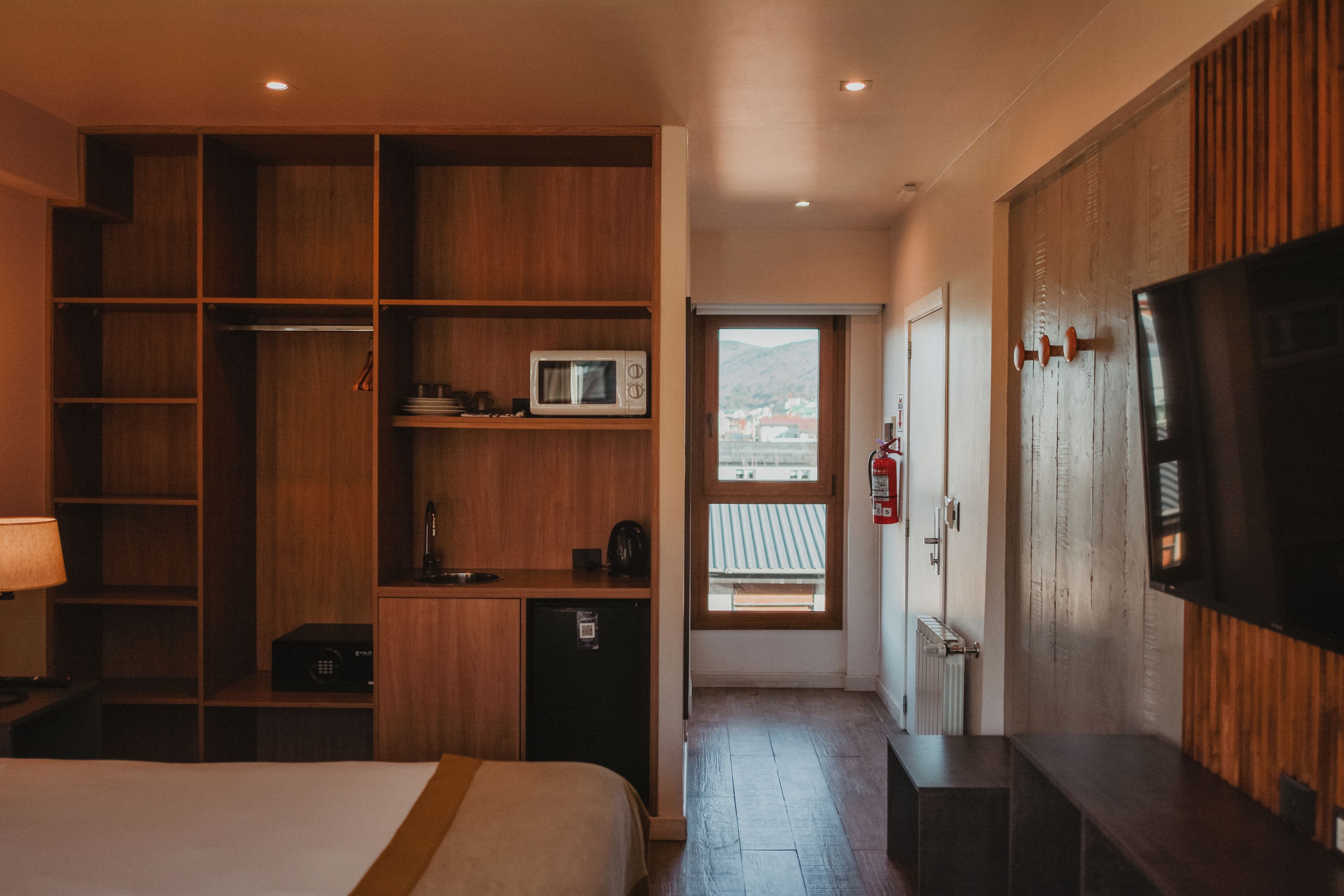 Habitación de hotel con cama, kitchenette, televisión y vistas a través de una ventana.