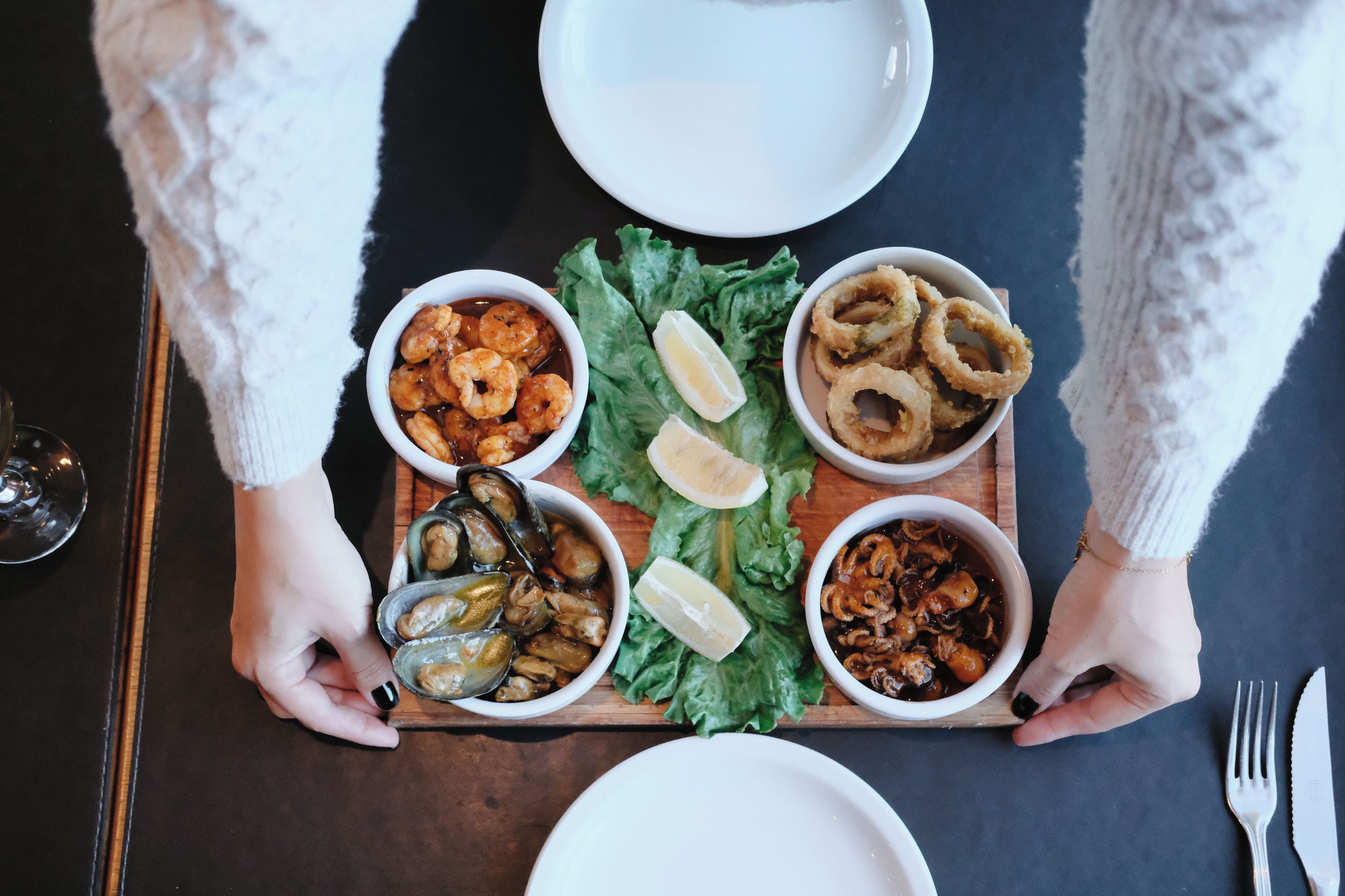 A meal tray with various seafood dishes, a glass of water, and a fork and knife on a table.