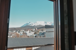 Une montagne aux sommets enneigés en arrière-plan, une ville avec différents bâtiments au premier plan et un cadre de fenêtre au premier plan.