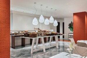 Uma zona de refeições moderna com chão de mármore, mesas brancas e um buffet com diversas opções de comida.
