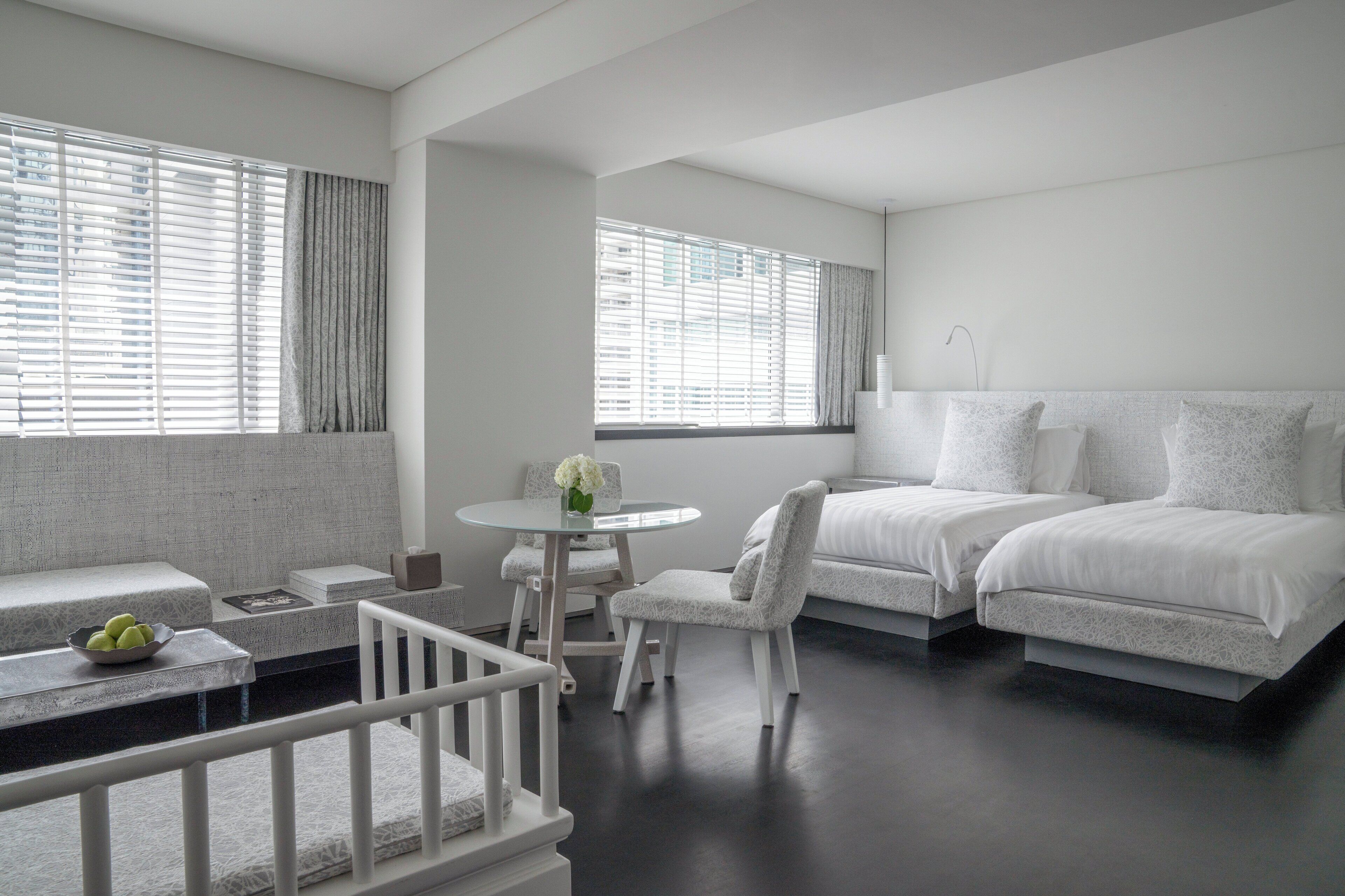 A modern hotel room with a bed, two chairs, a small table, and a balcony.