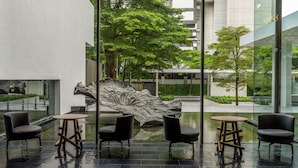 A modern outdoor seating area with a large metallic sculpture, surrounded by glass walls and trees. - COMO Metropolitan Bangkok (Bangkok)