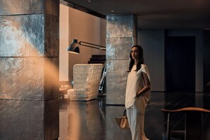 A person standing in a modern lobby with a stone column, a desk, and a lamp. - COMO Metropolitan Bangkok (Bangkok)