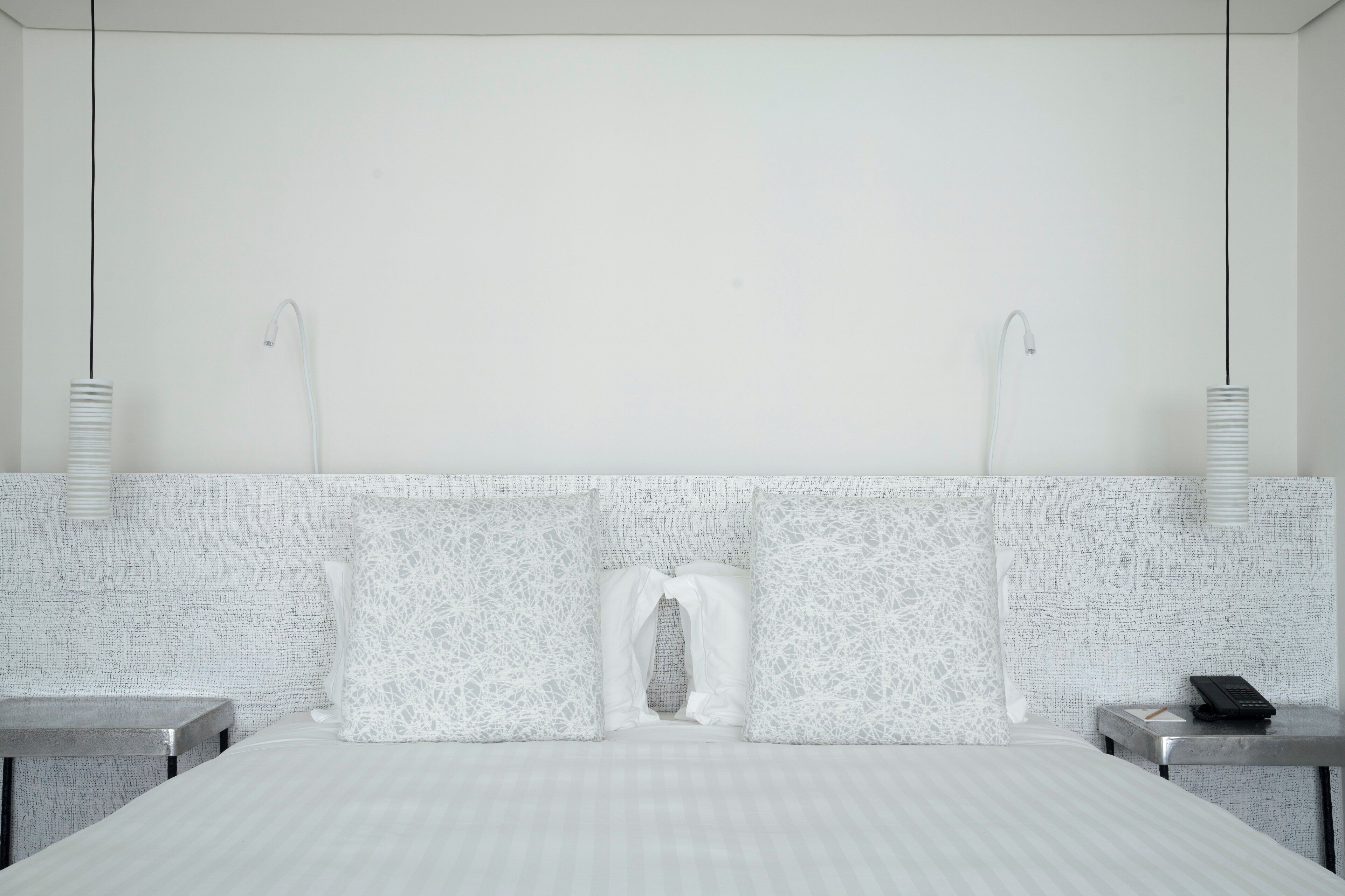 Una habitación de hotel moderna con una cama grande, dos mesitas de noche y un cabecero con textura.